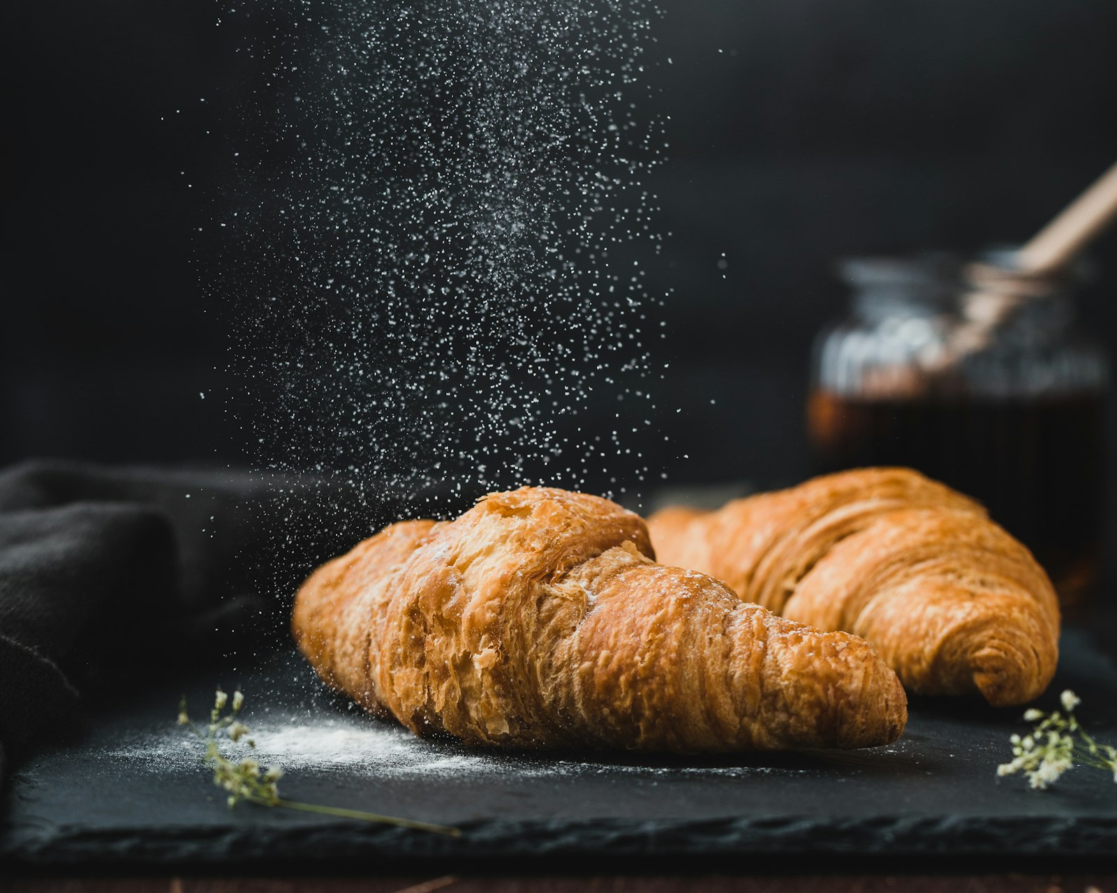 Croissants recién horneados con azúcar flor cayendo sobre fondo negro